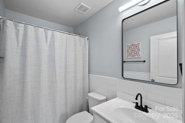 bathroom with a wainscoted wall, tile walls, visible vents, toilet, and vanity