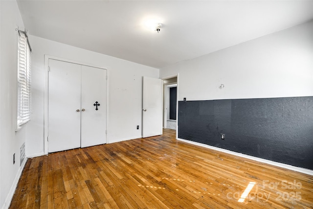 unfurnished bedroom featuring a closet, wood-type flooring, and baseboards