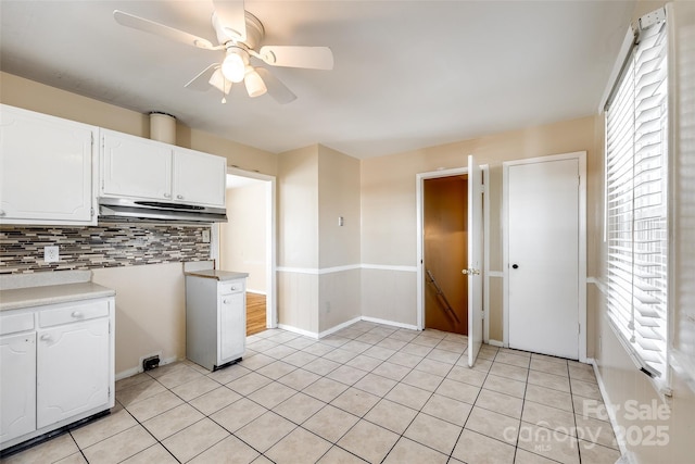 kitchen with tasteful backsplash, light tile patterned flooring, white cabinets, and under cabinet range hood