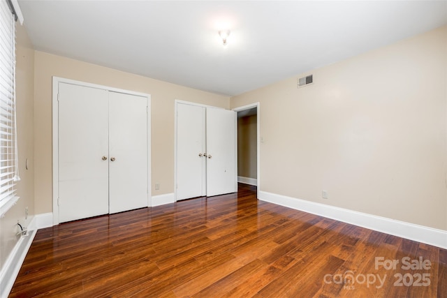 unfurnished bedroom featuring baseboards, visible vents, and wood finished floors