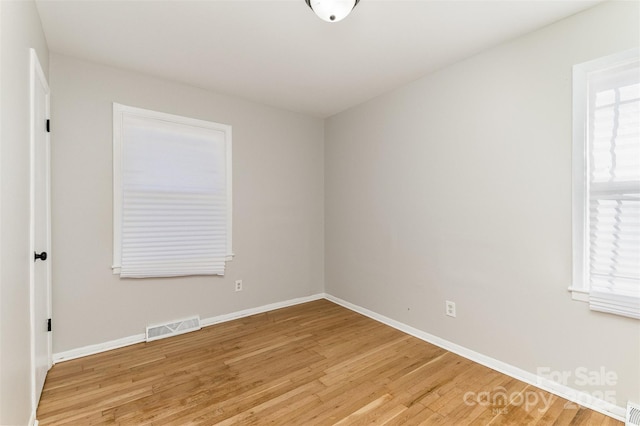 empty room with a healthy amount of sunlight, light wood-style floors, visible vents, and baseboards