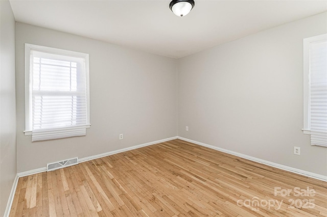 unfurnished room with visible vents, wood-type flooring, and baseboards