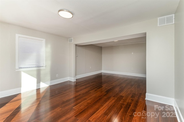 spare room with visible vents, baseboards, and dark wood finished floors