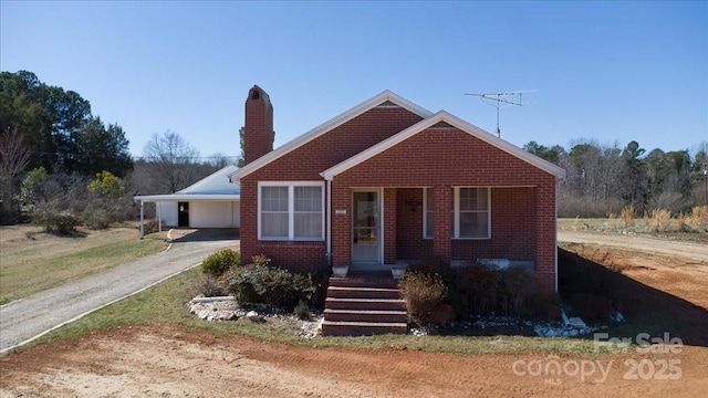 bungalow with a carport, brick siding, driveway, and a chimney