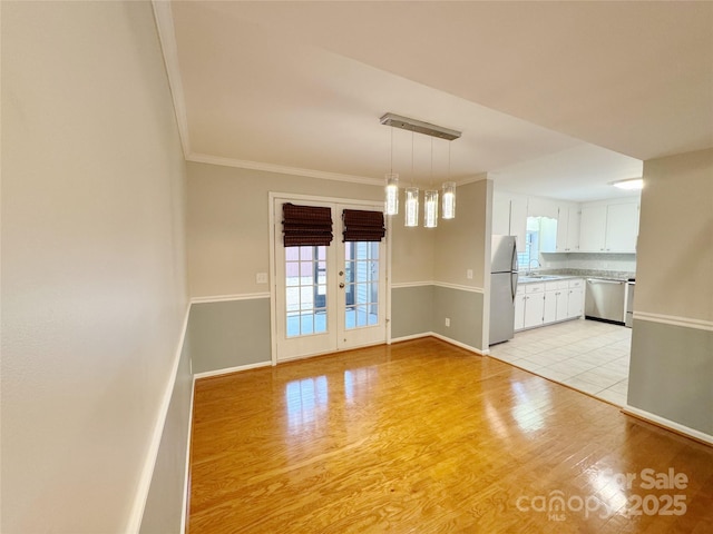 interior space with french doors, crown molding, a sink, light wood-type flooring, and baseboards