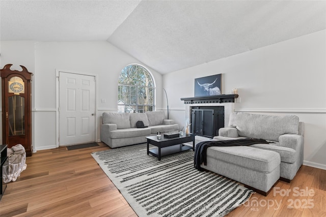 living area with vaulted ceiling, a fireplace, light wood finished floors, and a textured ceiling