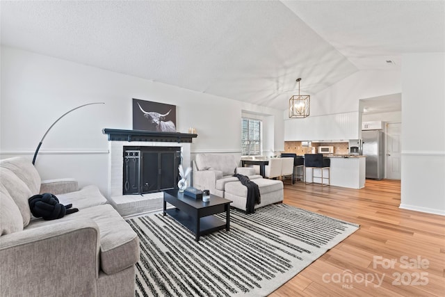 living room featuring light wood finished floors, vaulted ceiling, a fireplace, an inviting chandelier, and a textured ceiling