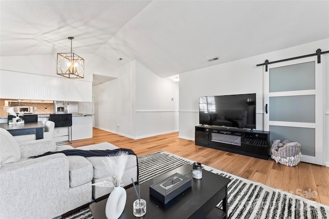 living area featuring visible vents, wood finished floors, a barn door, an inviting chandelier, and vaulted ceiling