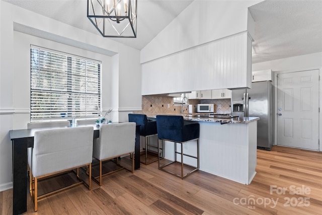 kitchen with a peninsula, stainless steel fridge with ice dispenser, light wood-style floors, and white microwave