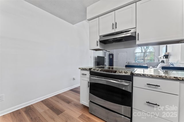 kitchen with electric range, under cabinet range hood, light stone counters, white cabinetry, and light wood-style floors