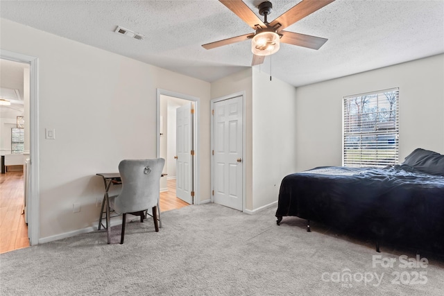 carpeted bedroom with visible vents, a textured ceiling, ensuite bathroom, and baseboards