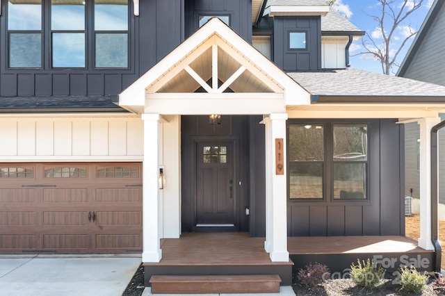 doorway to property featuring board and batten siding, concrete driveway, roof with shingles, and a garage