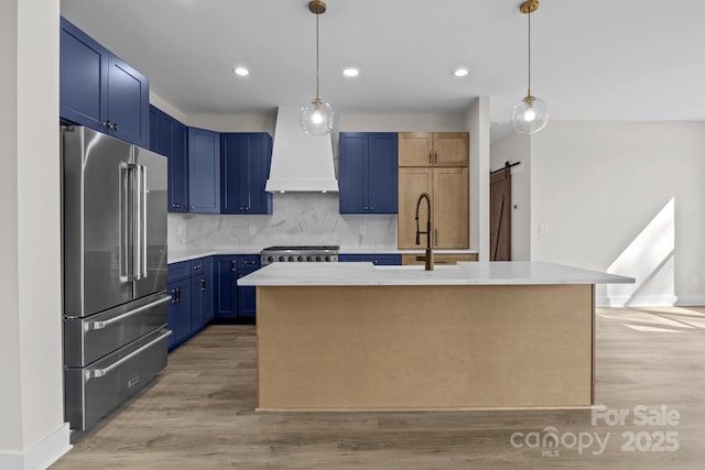 kitchen featuring a barn door, high end refrigerator, custom exhaust hood, blue cabinetry, and a sink