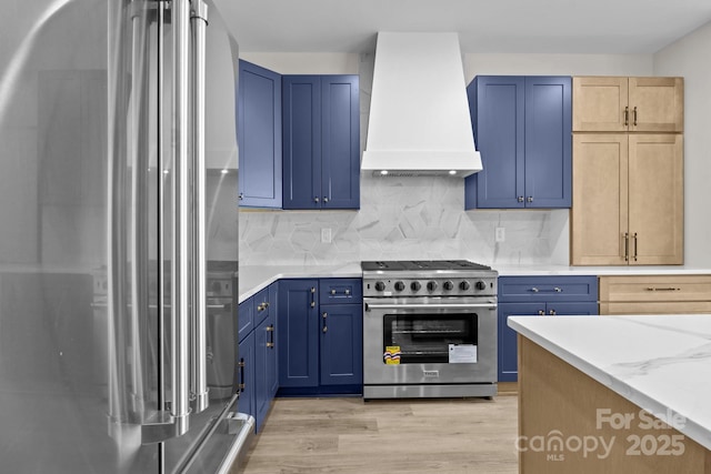 kitchen with blue cabinetry, custom range hood, stainless steel appliances, and decorative backsplash