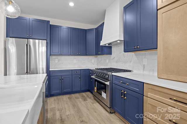 kitchen featuring blue cabinets, premium range hood, high end appliances, and backsplash