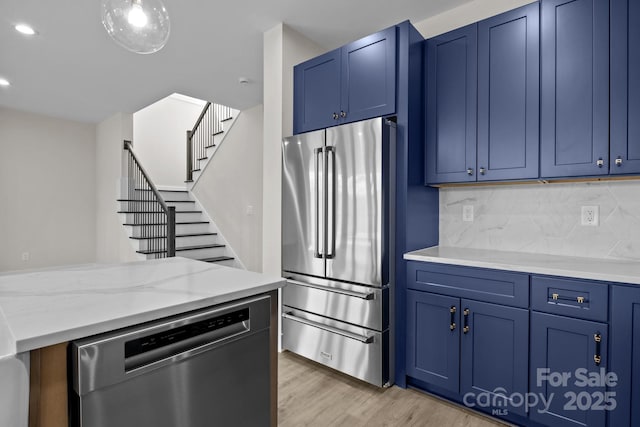 kitchen featuring blue cabinets, light wood-style flooring, appliances with stainless steel finishes, and tasteful backsplash