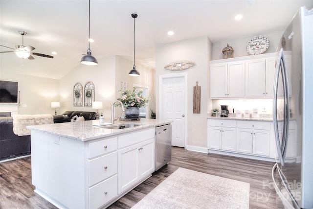 kitchen with light stone counters, a sink, appliances with stainless steel finishes, white cabinetry, and open floor plan