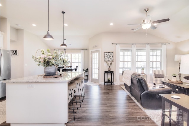 kitchen featuring a breakfast bar area, light stone countertops, freestanding refrigerator, vaulted ceiling, and dark wood-type flooring