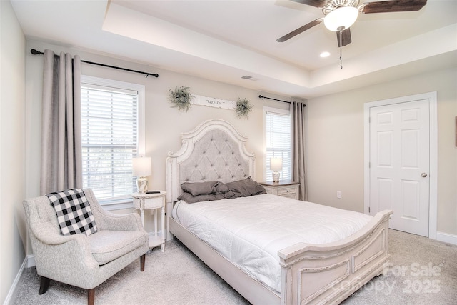 bedroom featuring baseboards, multiple windows, a raised ceiling, and light carpet