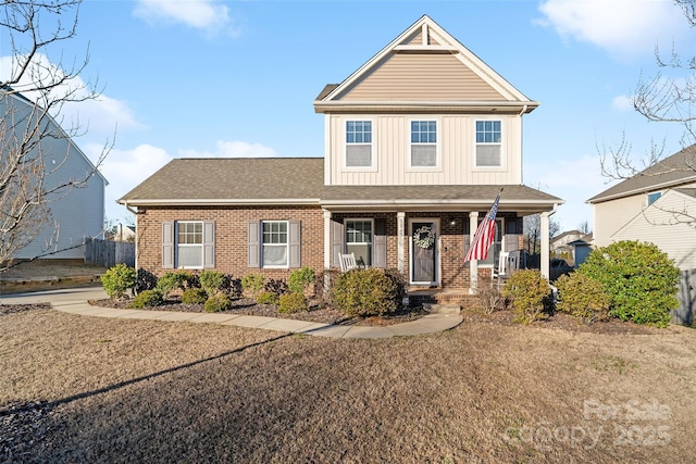 view of front of house with a shingled roof, covered porch, a front lawn, board and batten siding, and brick siding