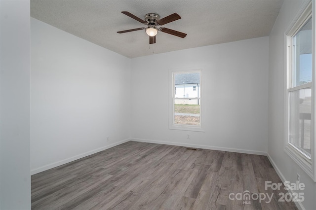 unfurnished room with a textured ceiling, baseboards, and wood finished floors