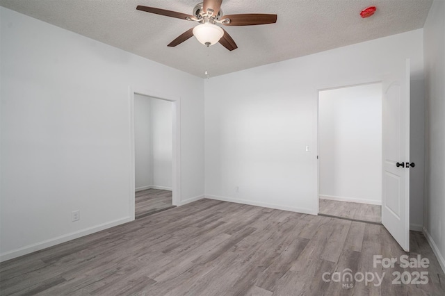 empty room featuring a textured ceiling, ceiling fan, wood finished floors, and baseboards