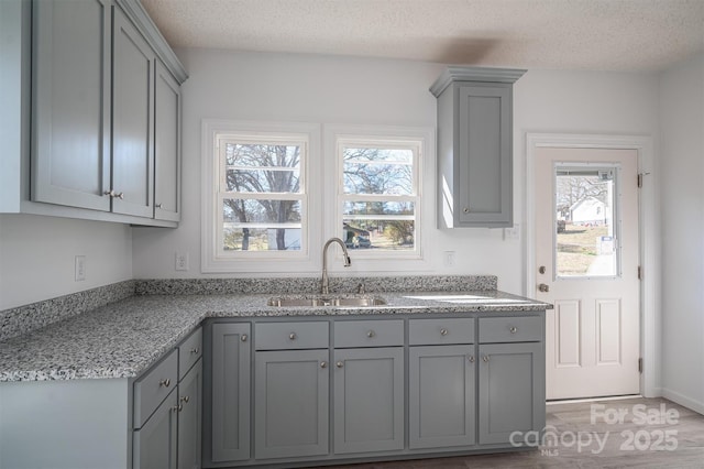 kitchen with a textured ceiling, light stone counters, gray cabinets, and a sink