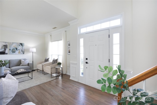 entryway featuring visible vents, ornamental molding, a decorative wall, and wood finished floors