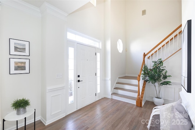 entryway with stairway, wood finished floors, a towering ceiling, and a decorative wall