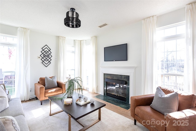 living room featuring a fireplace with flush hearth, a textured ceiling, visible vents, and wood finished floors