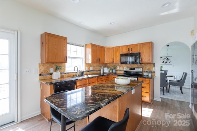 kitchen with black appliances, light wood-style flooring, arched walkways, and decorative backsplash