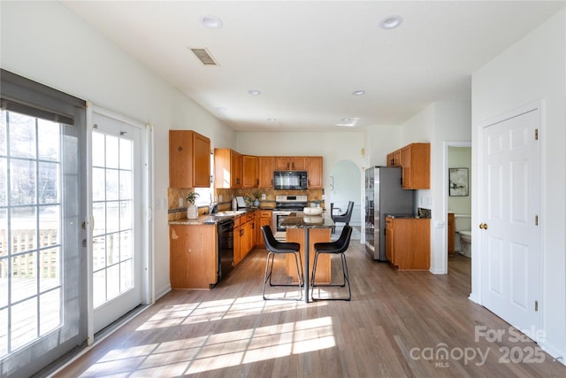 kitchen with tasteful backsplash, visible vents, brown cabinetry, arched walkways, and black appliances