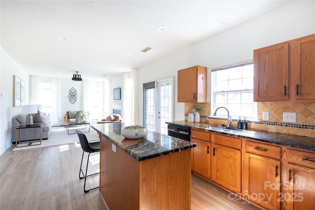 kitchen featuring dark stone counters, brown cabinetry, a kitchen island, light wood-style floors, and a sink