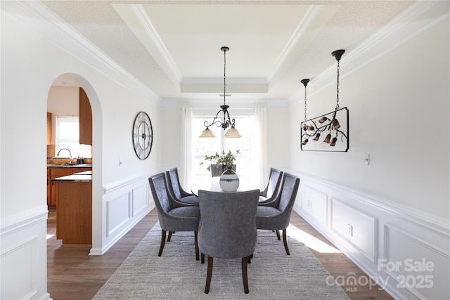 dining room featuring arched walkways, dark wood finished floors, a tray ceiling, crown molding, and a decorative wall