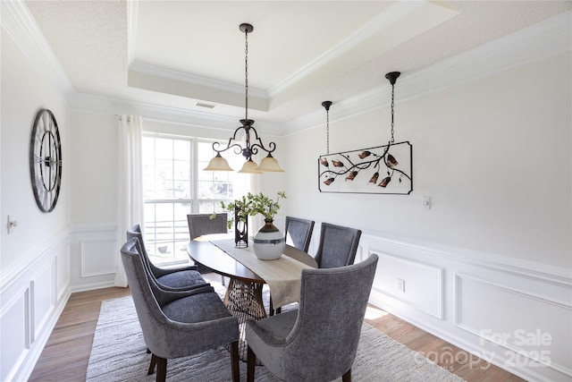 dining space featuring wood finished floors, a raised ceiling, visible vents, and a decorative wall