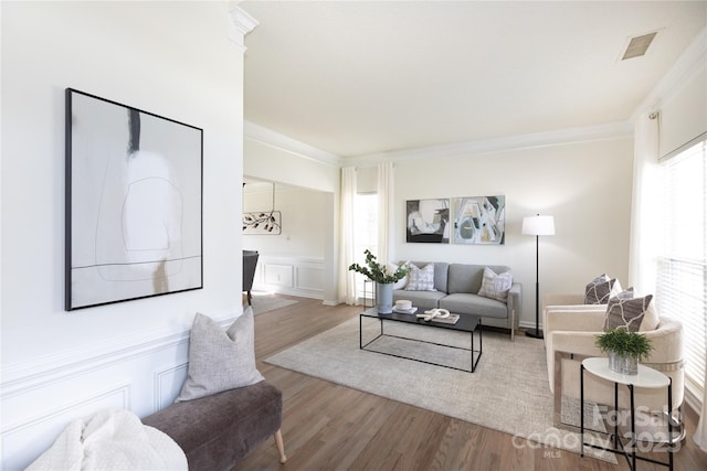 living room with ornamental molding, wood finished floors, visible vents, and a decorative wall