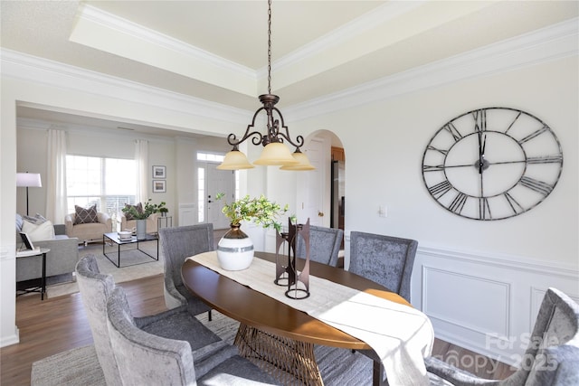 dining area featuring arched walkways, a tray ceiling, wood finished floors, and crown molding