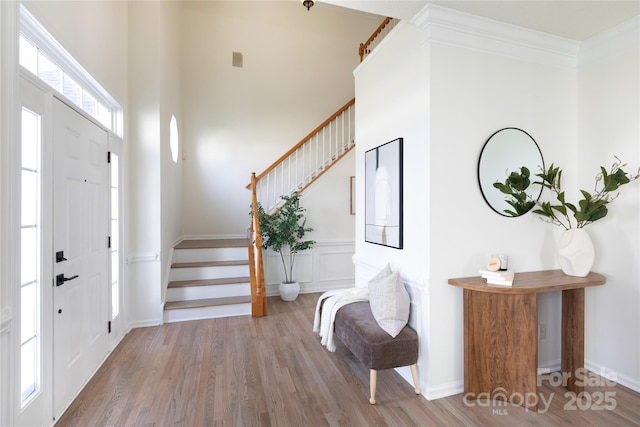 entrance foyer featuring baseboards, ornamental molding, wood finished floors, stairs, and a high ceiling