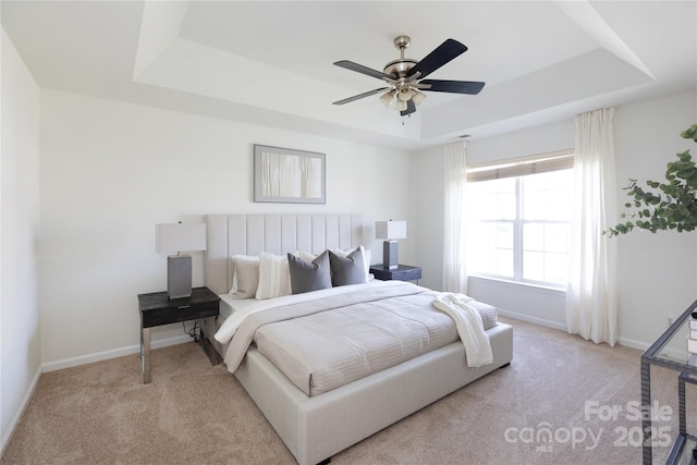 carpeted bedroom with a tray ceiling, a ceiling fan, and baseboards