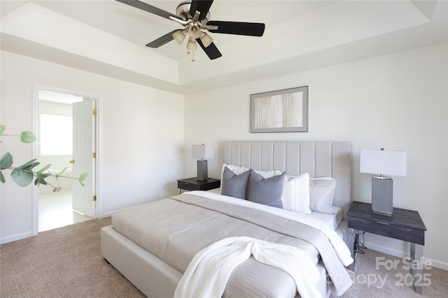 carpeted bedroom featuring a tray ceiling, a ceiling fan, and baseboards