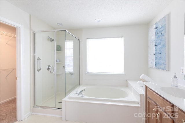 full bath with a textured ceiling, vanity, a spacious closet, a bath, and a stall shower