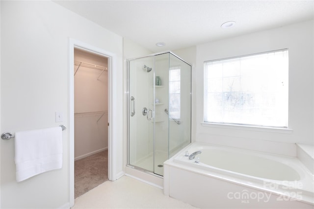 bathroom featuring a walk in closet, a garden tub, and a shower stall