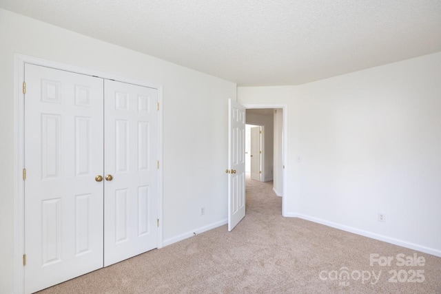 unfurnished bedroom featuring a closet, light carpet, a textured ceiling, and baseboards