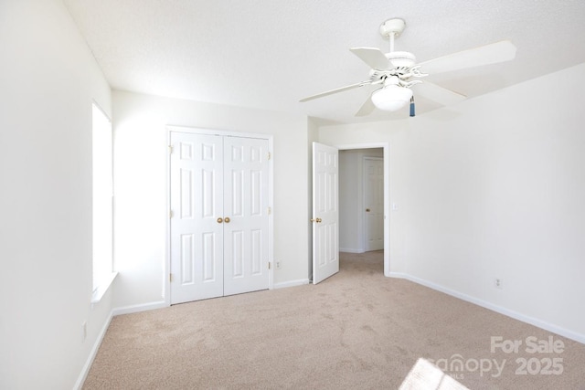 unfurnished bedroom with carpet floors, a closet, baseboards, and a ceiling fan