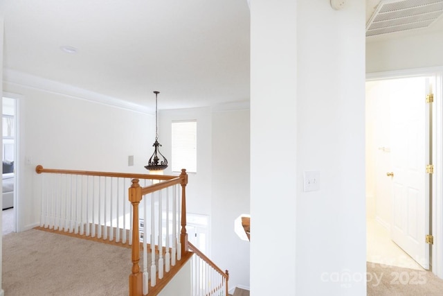 hallway with carpet, visible vents, crown molding, and an upstairs landing