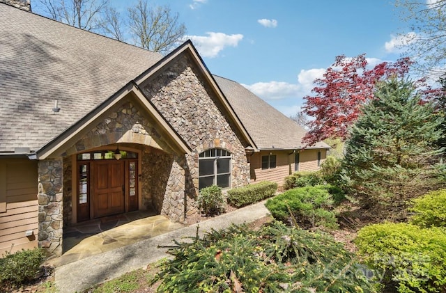 view of exterior entry featuring stone siding and roof with shingles