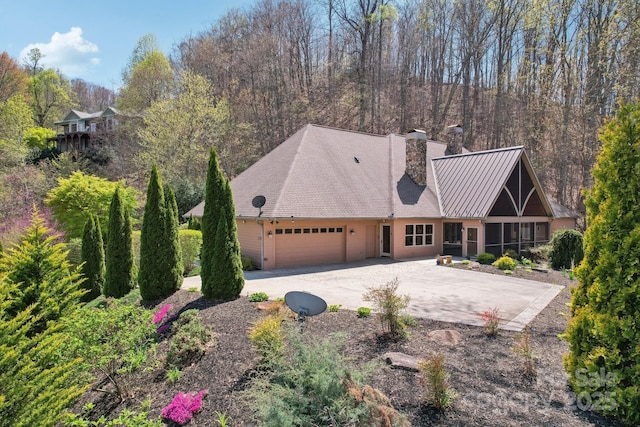 view of front of home featuring a chimney, concrete driveway, an attached garage, a sunroom, and metal roof