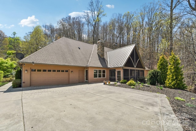 view of front of property with concrete driveway, a chimney, an attached garage, metal roof, and a sunroom
