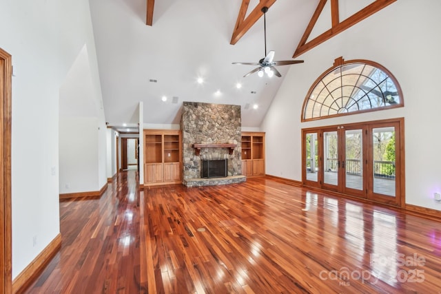 unfurnished living room with high vaulted ceiling, ceiling fan, beamed ceiling, a fireplace, and wood-type flooring