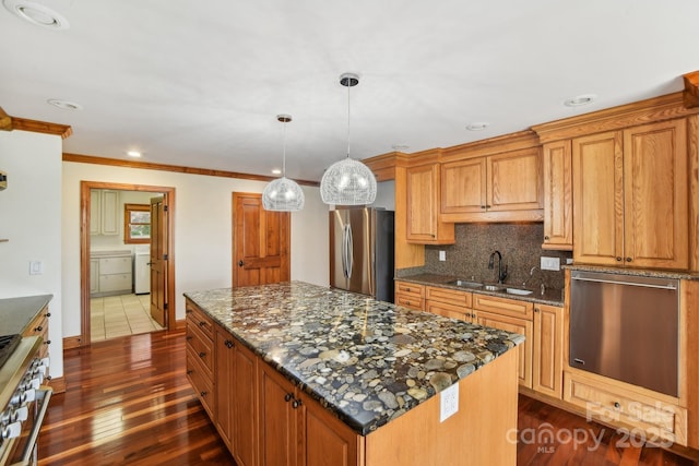 kitchen featuring a sink, decorative backsplash, stainless steel appliances, washing machine and dryer, and a kitchen island